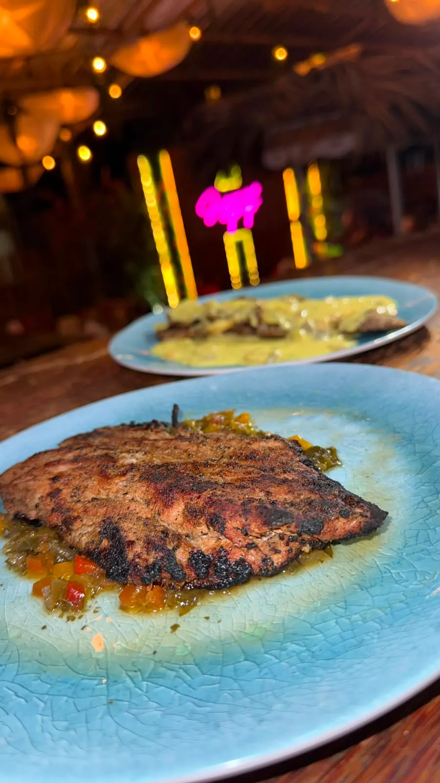 Churrasco a la parrilla servido sobre vegetales salteados en un plato azul.