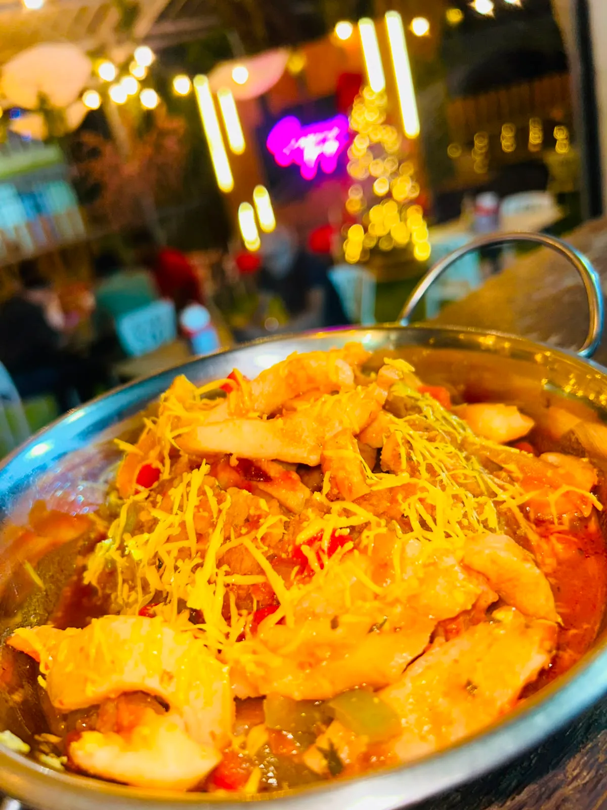 Cazuela de camarones guisados con queso, frente a luces festivas.