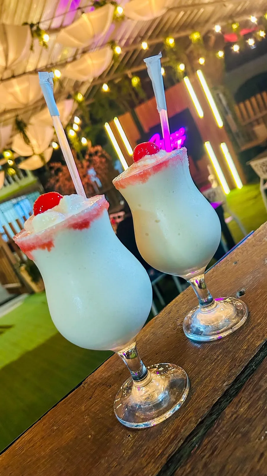 Piña colada cremosa con cereza, servida bajo las luces del patio.