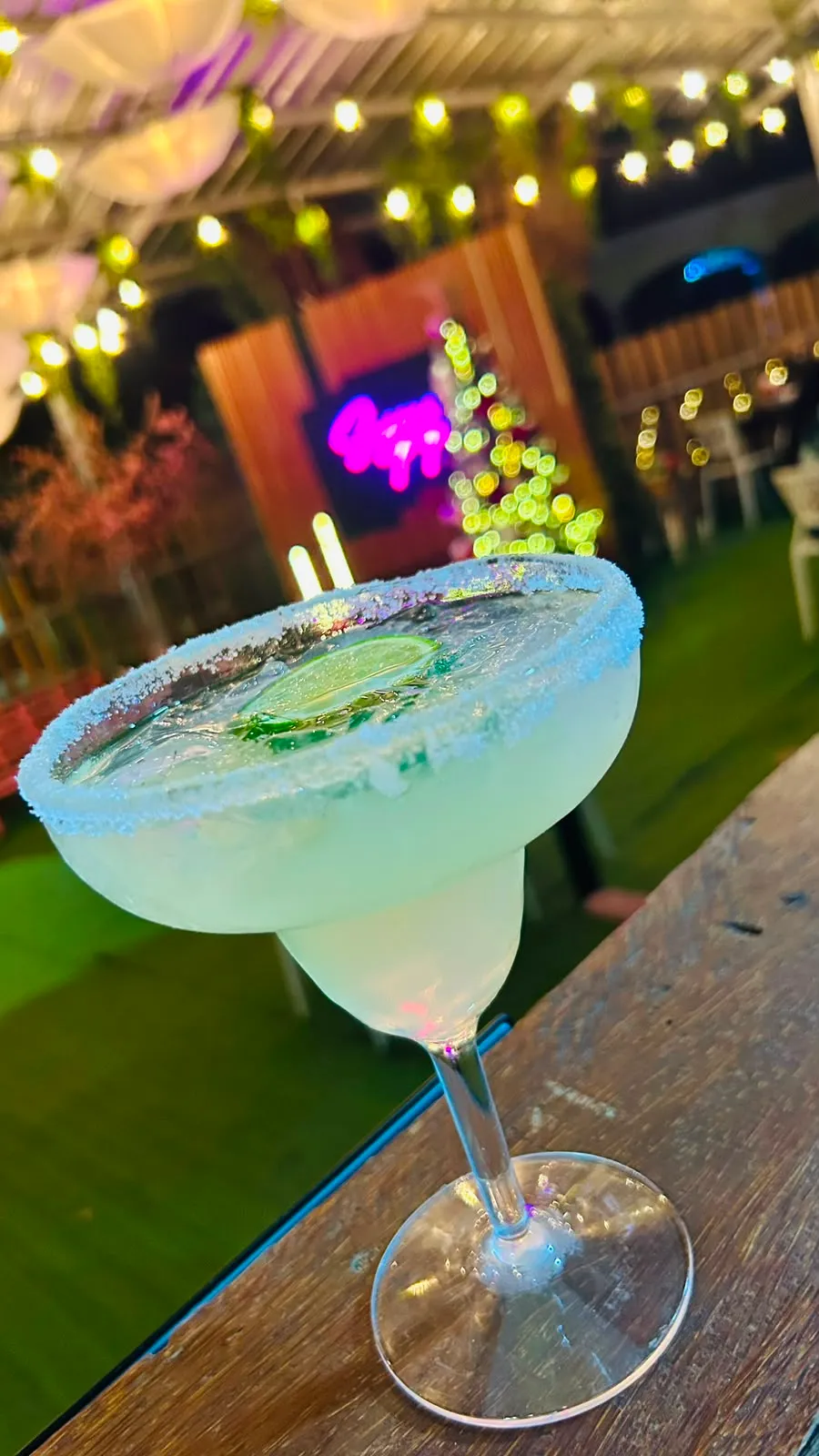 Margarita con borde de sal y rodaja de limón frente a luces festivas.