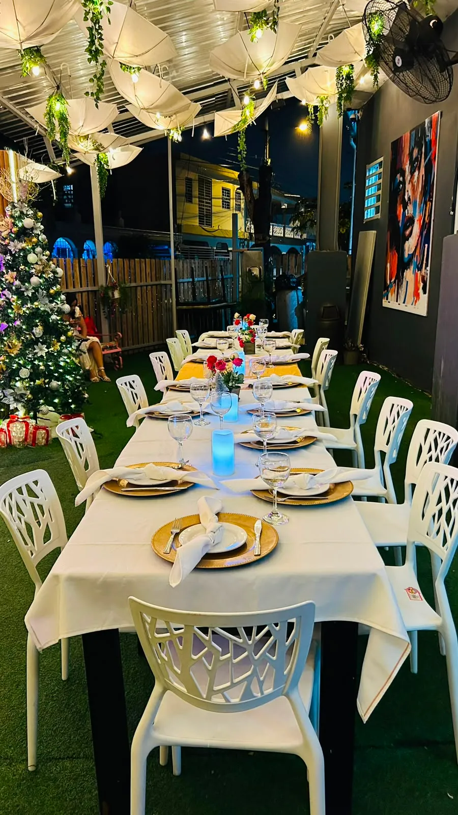 Mesa montada con vajilla dorada bajo el techo de luces del patio de Sazonao Pop, junto a un árbol iluminado.